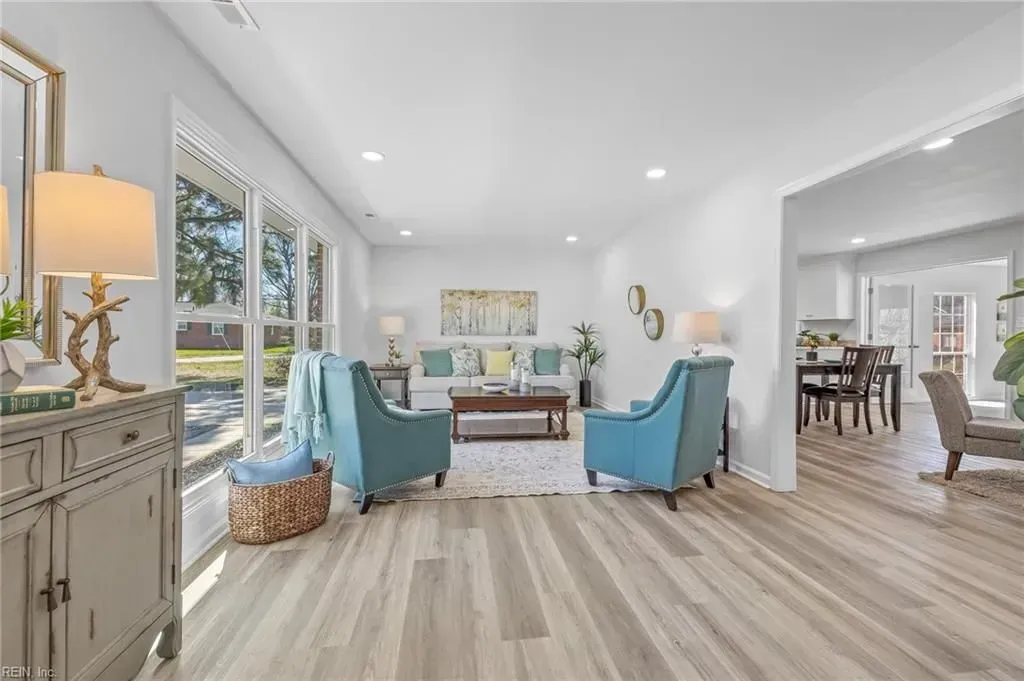 Bright, modern living room with blue armchairs, a white sofa, and light wood floors.