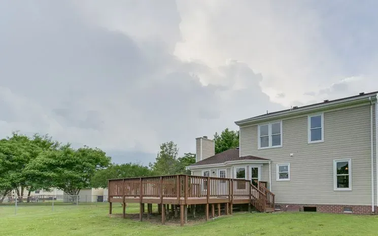 Backyard with a wooden deck, a light-colored house, and a cloudy sky.