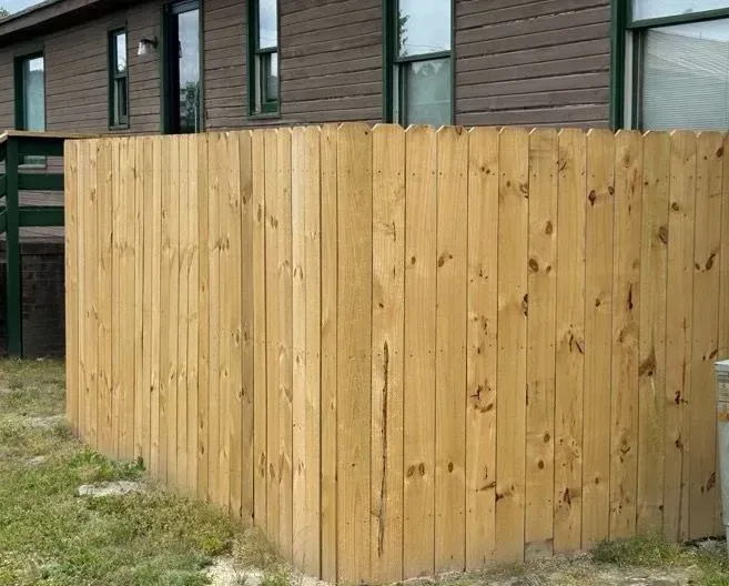 Wooden fence in front of a brown building, on a grassy patch.