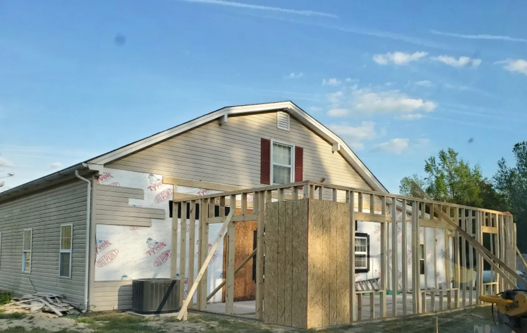House under construction with framed walls, OSB sheathing, and exterior siding against a blue sky.