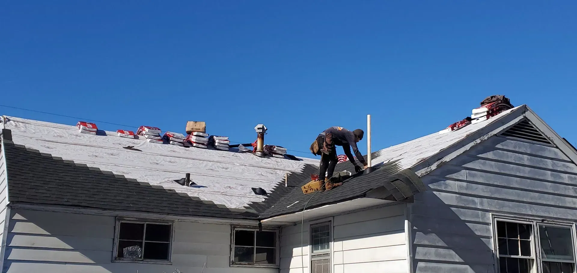 Roofer working on a house roof under a clear blue sky.