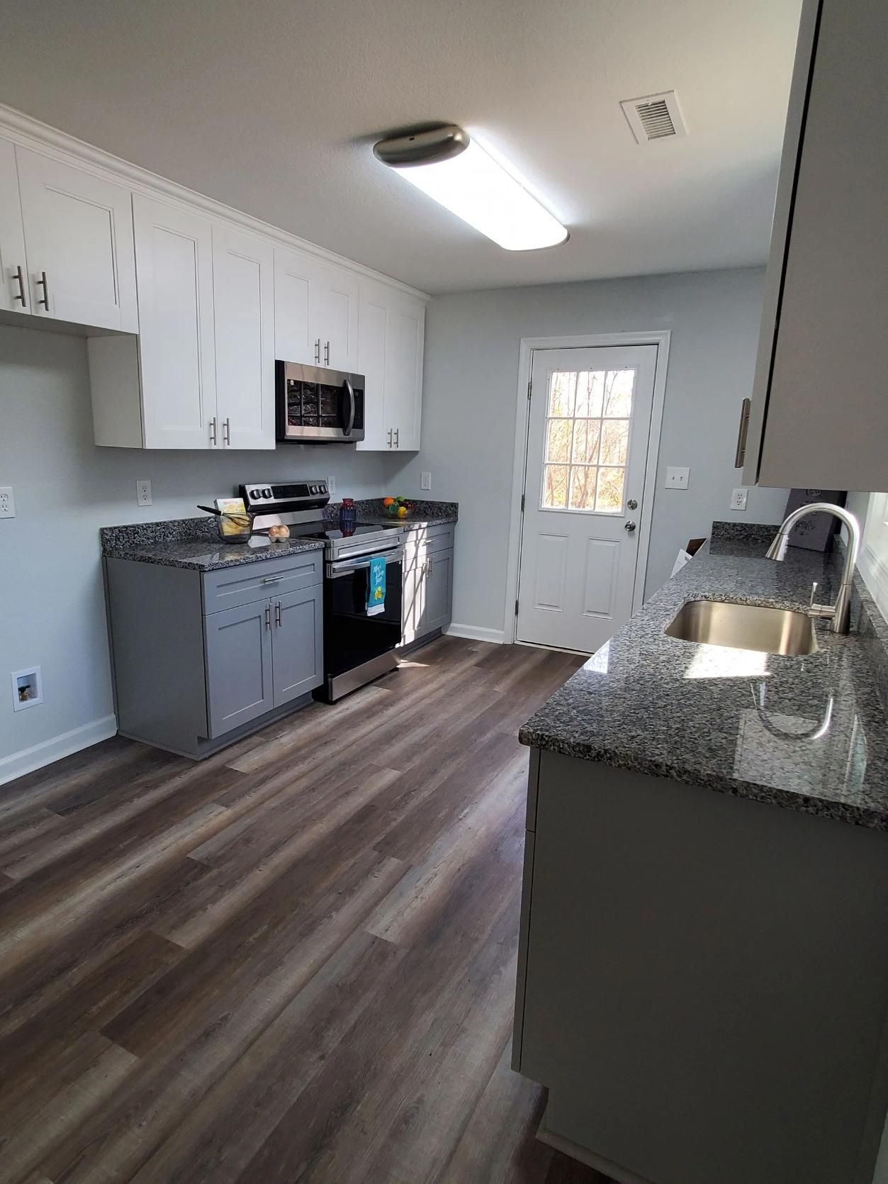 Kitchen with gray and white cabinets, granite countertops, stainless steel appliances, and wood-look flooring.