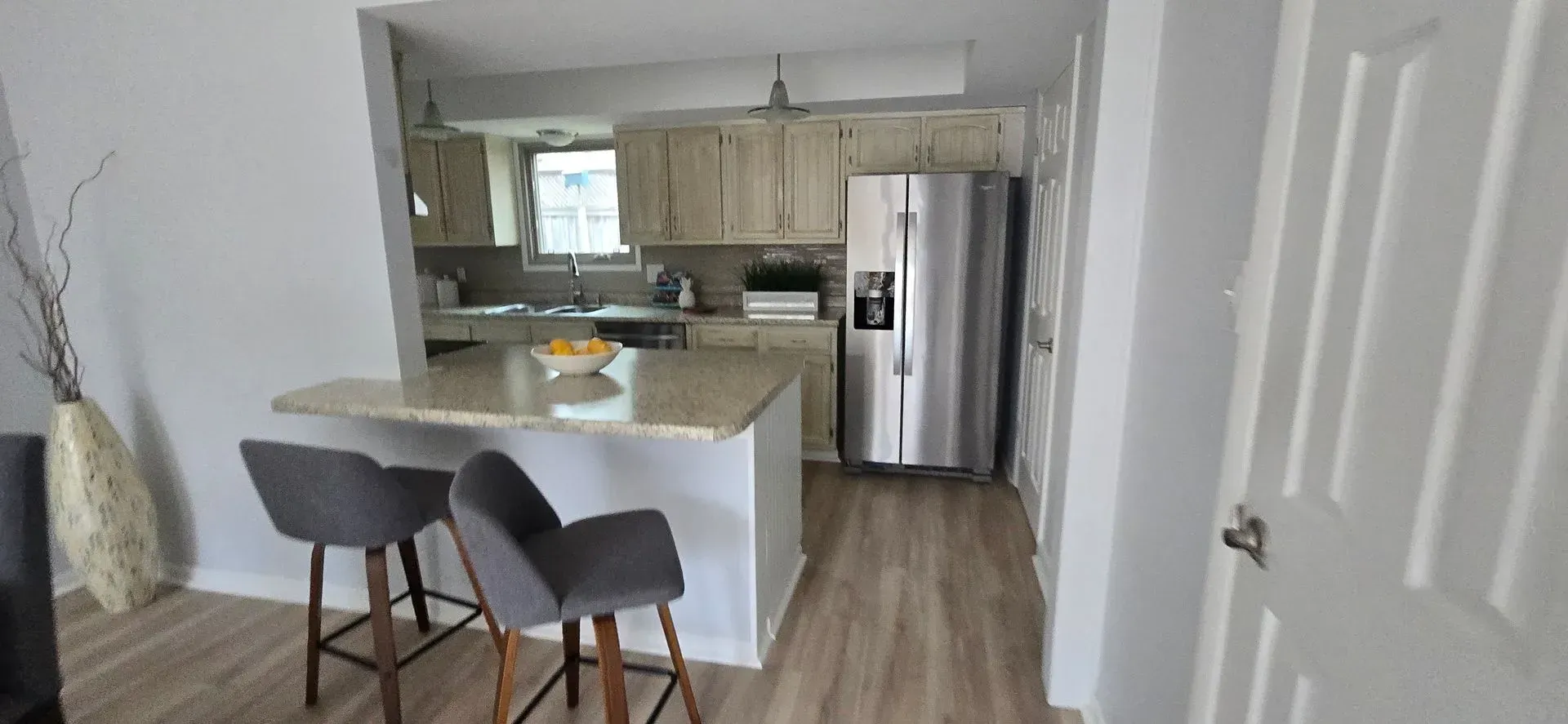 Kitchen interior with a breakfast bar, gray stools, and stainless steel refrigerator.