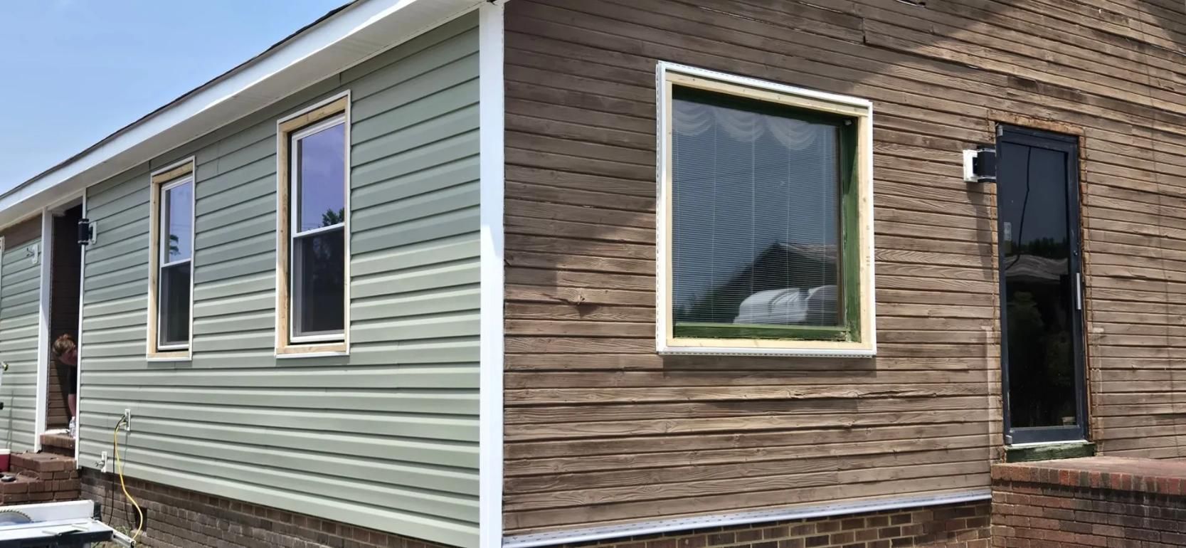 Two-tone house exterior: green siding and brick, with windows and a black shutter.
