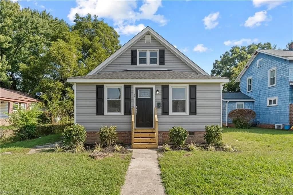 Gray house with black shutters and door, small wooden porch. Sunny day.