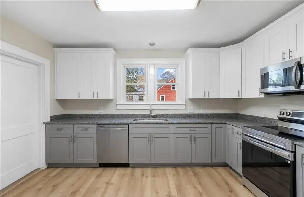 Kitchen with light wood floor, gray and white cabinets, stainless steel appliances, and a window.
