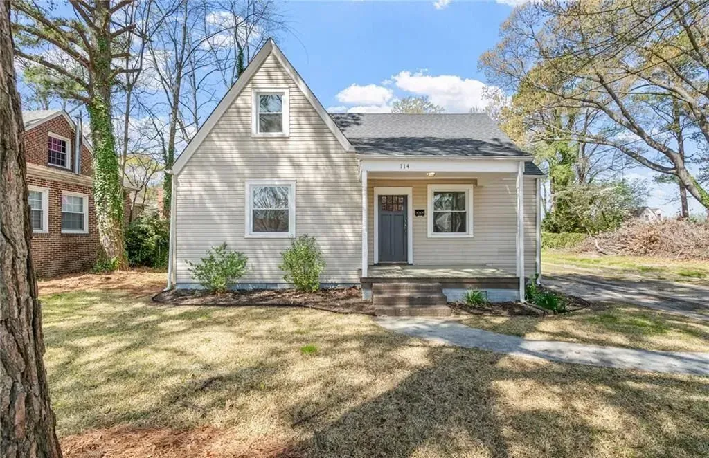 Small beige house with gray door, steps, and front yard.
