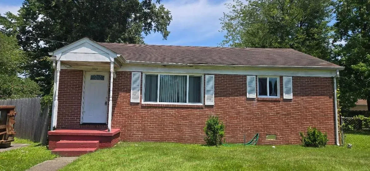 Red brick house with a white door, white window shutters, and a green lawn.