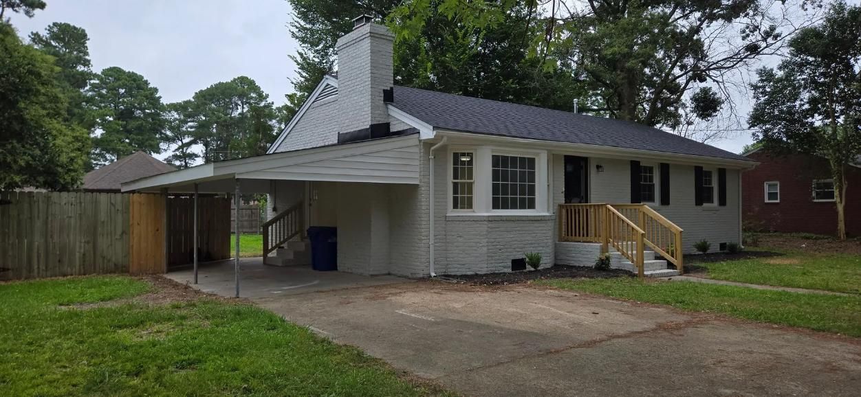 Gray house with carport, chimney, and wooden stairs. 