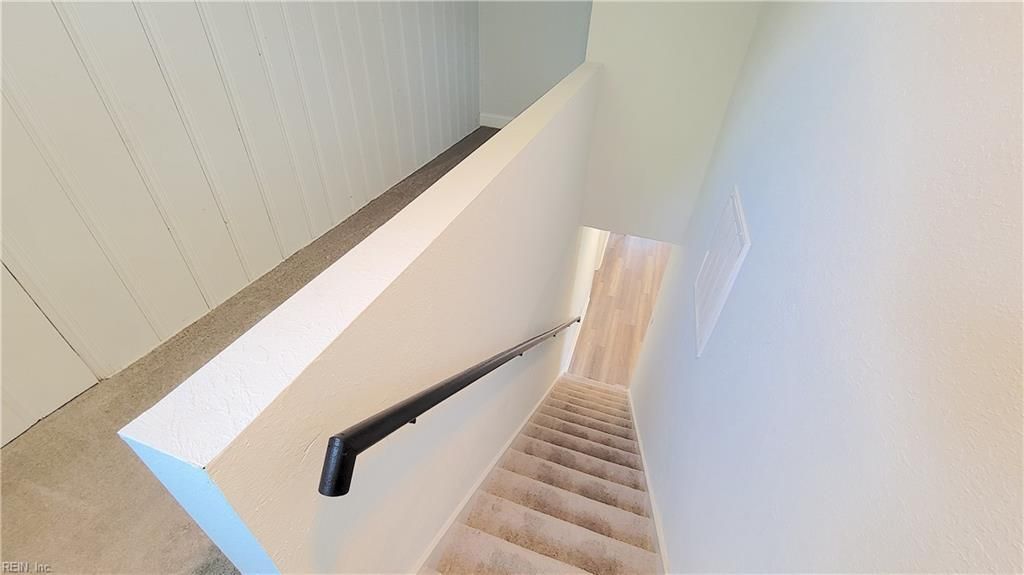 Staircase with light-colored carpet, white walls, and a black handrail descending from an upper level.