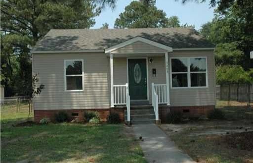 Tan bungalow with white trim, green door, and small porch. Sidewalk leads to the entrance.