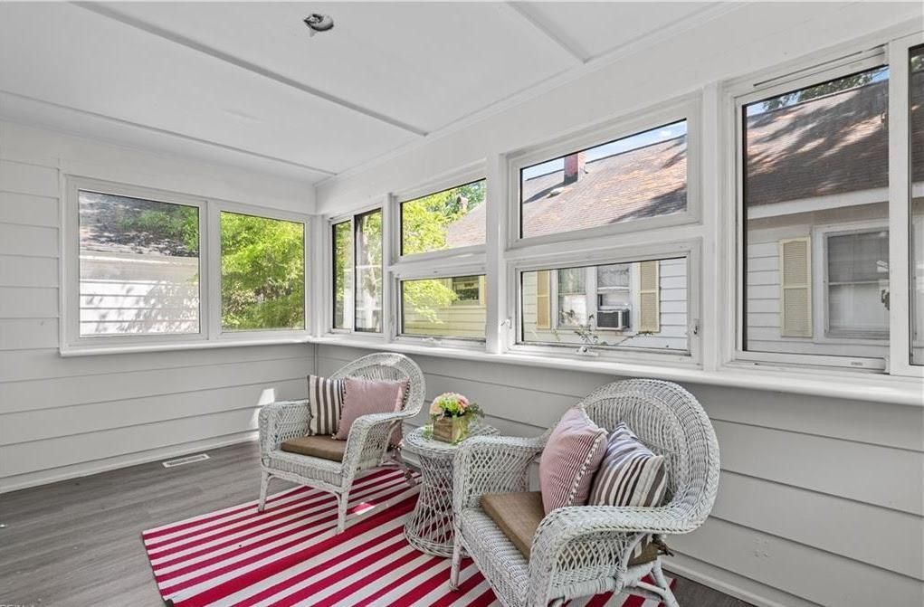 Bright sunroom with wicker chairs, striped rug, and large windows overlooking a neighborhood.