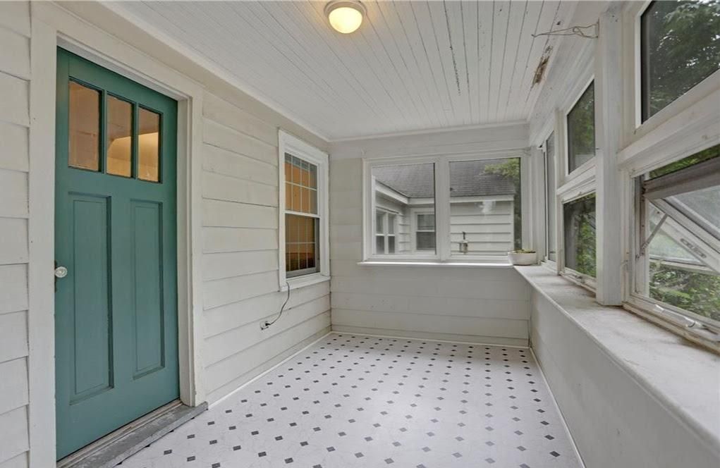 Enclosed porch with a teal door, windows, and patterned floor. White siding and ceiling.