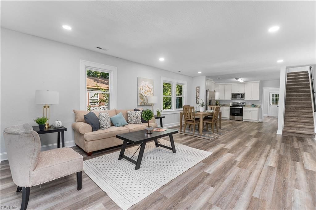 Spacious, open-plan living area with light wood floors, sofa, dining table, and stairs to upper level.