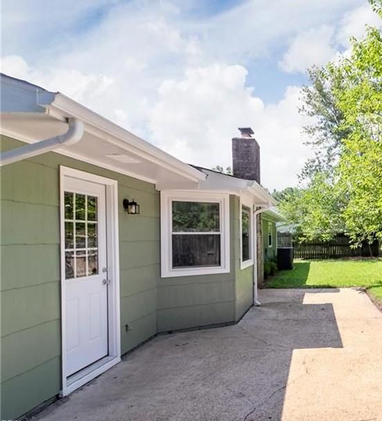Green house exterior with white door, window, concrete patio, and chimney against a blue sky.