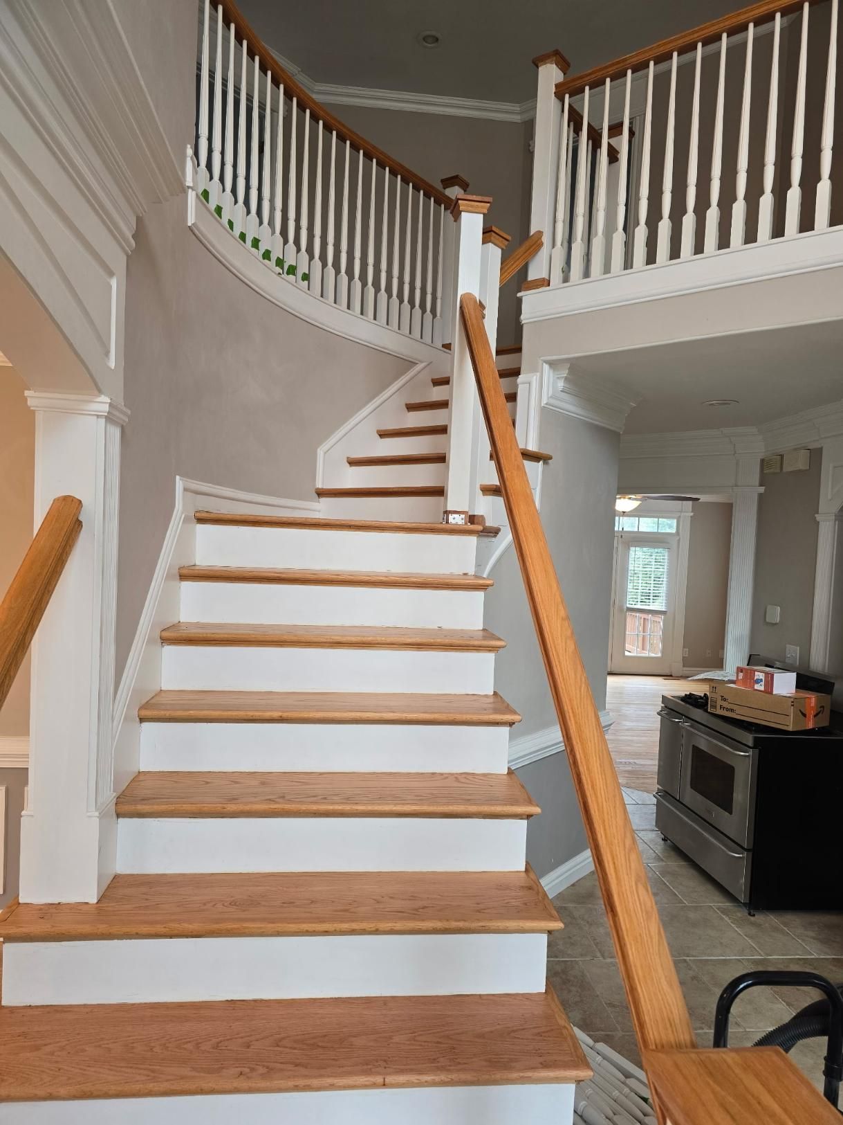 Wooden staircase with white risers and tan handrails, leading to a second floor.