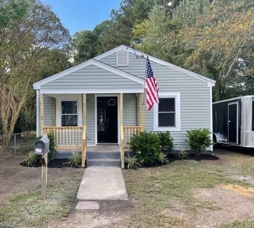 Small, light green house with porch and American flag, set in a yard with trees.