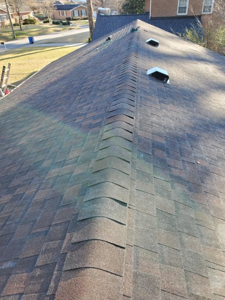 Dark roof with brown and black shingles, three vents, and a slight sunlight reflection.