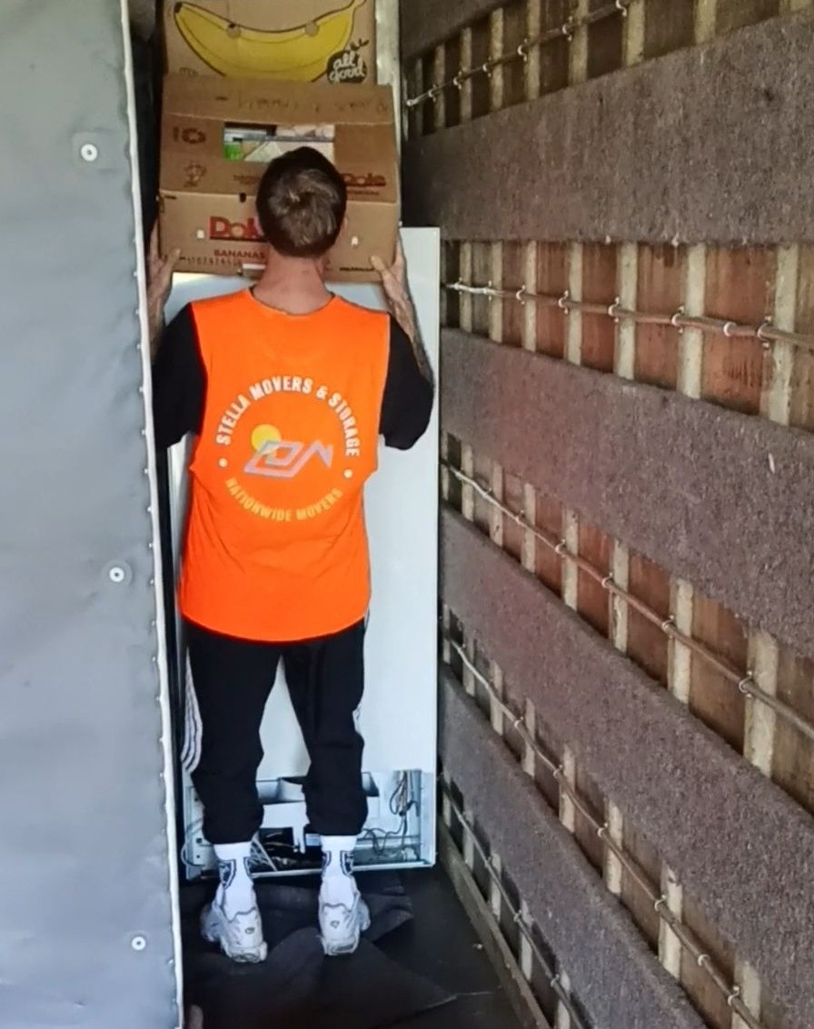 A moving man loading boxes into a truck from a house, sunny day. A moving man loading boxes into a truck from a house, sunny day.