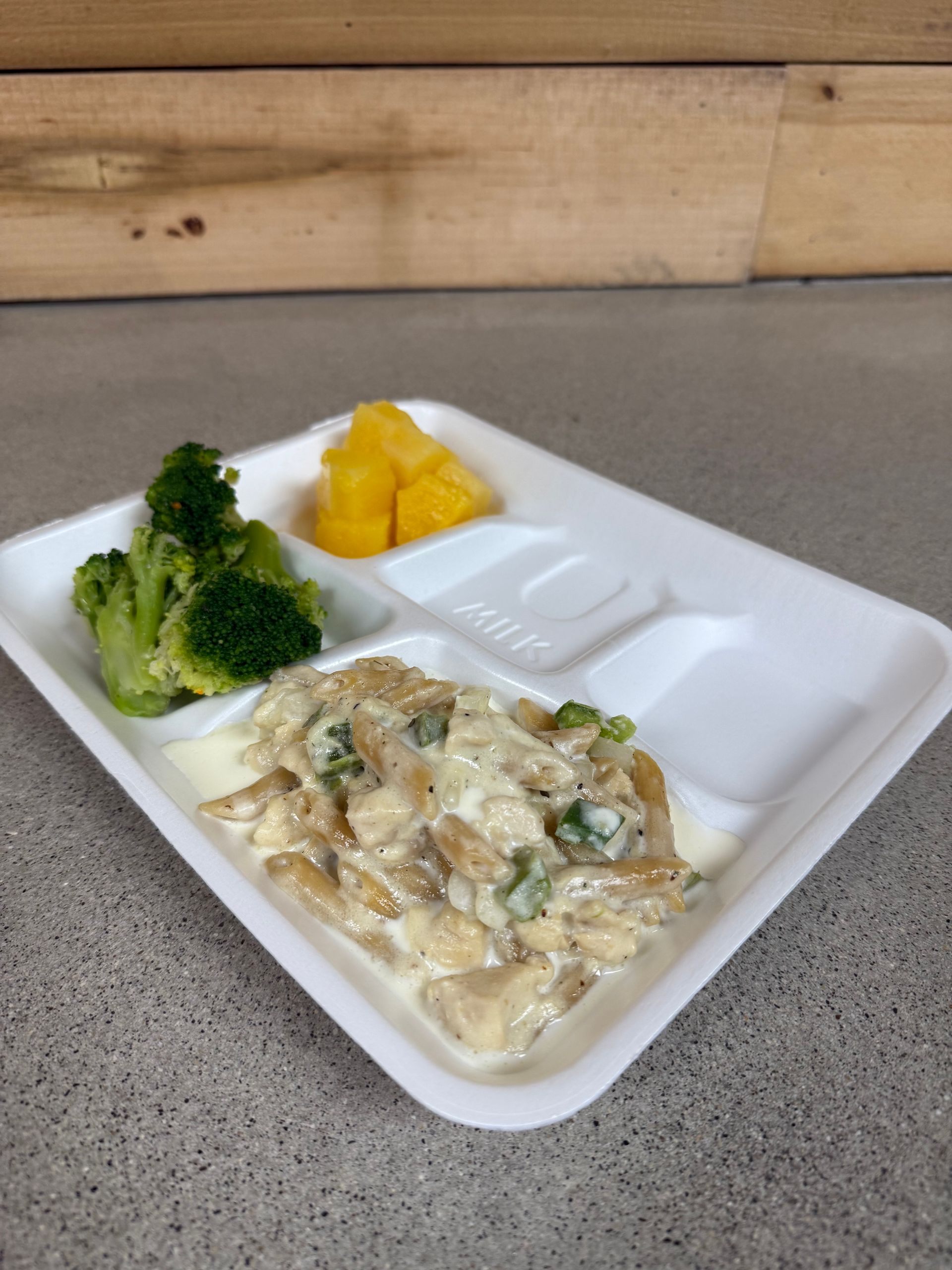 A styrofoam tray with broccoli and chicken on it