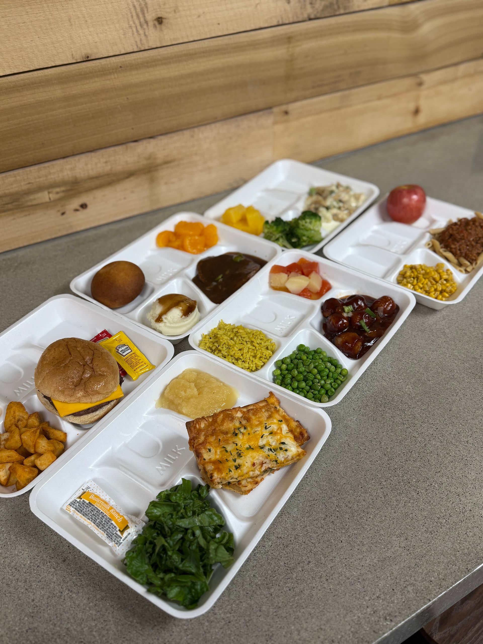 A row of styrofoam trays filled with different types of food.