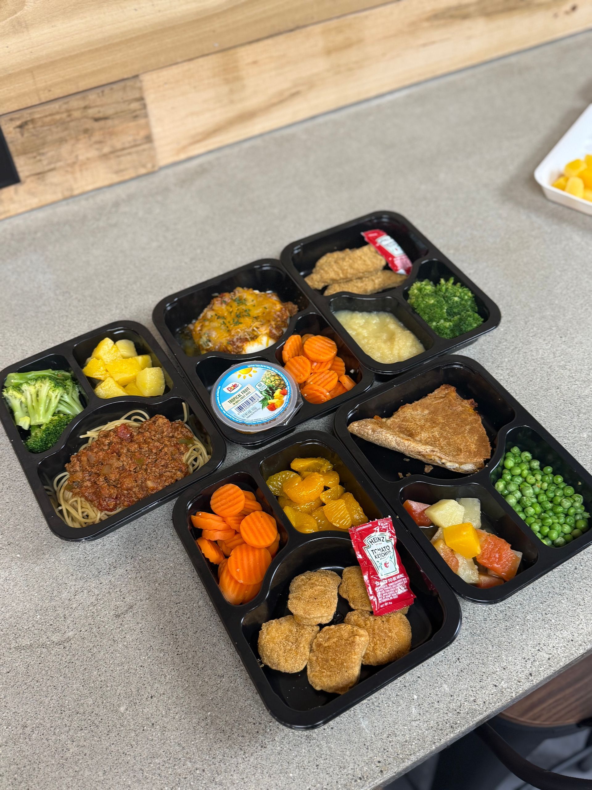 Several trays of food are sitting on a counter.