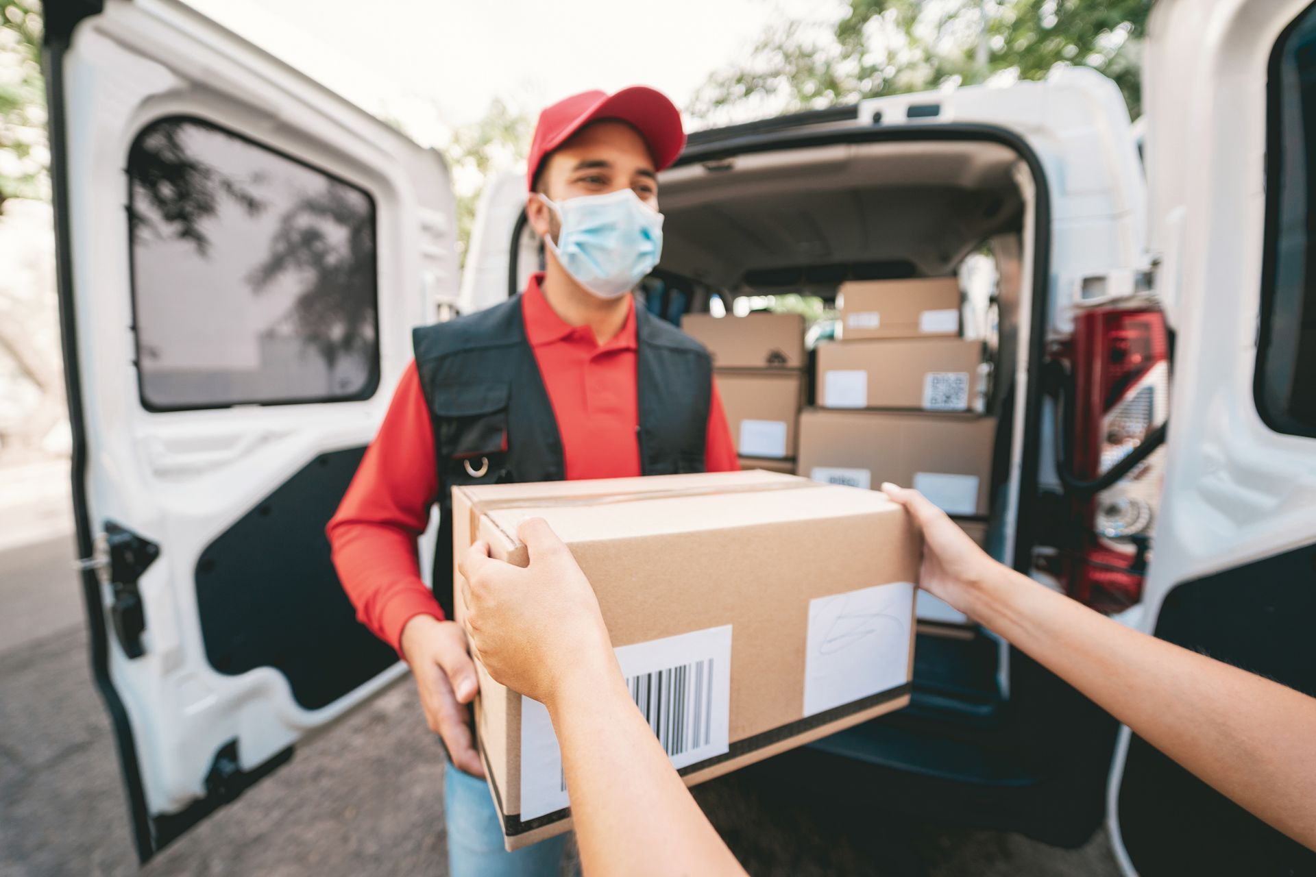 A delivery man wearing a mask is handing a box to a woman.