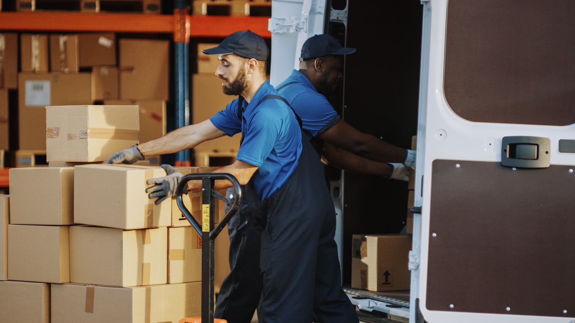 Two delivery men are loading boxes into a van in a warehouse.