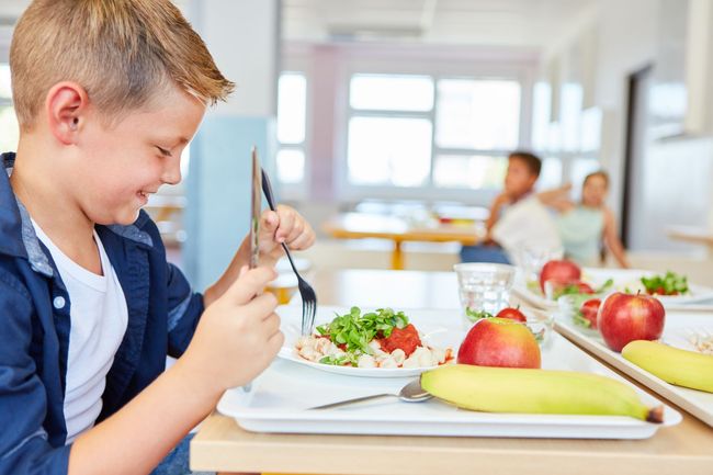 A young boy is sitting at a table eating food from a tray.