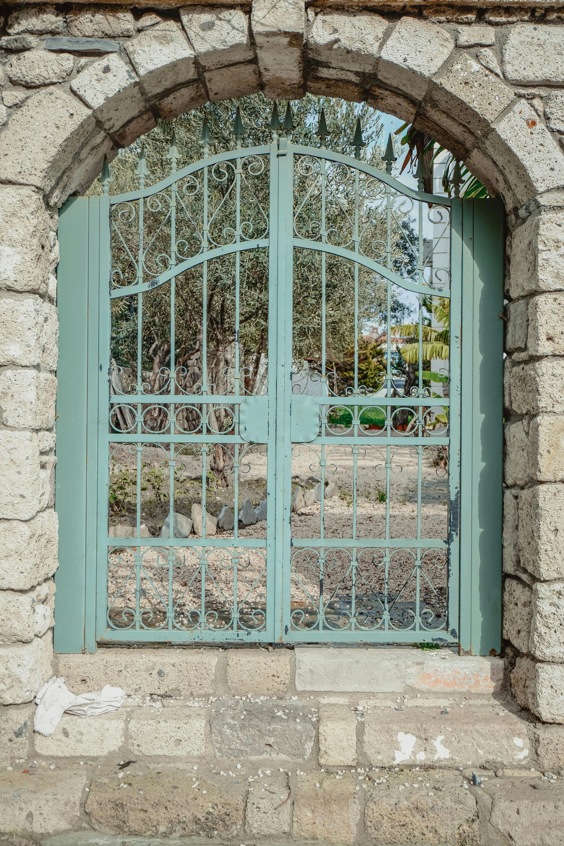 Green metal gate in stone archway, trees visible behind the gate.