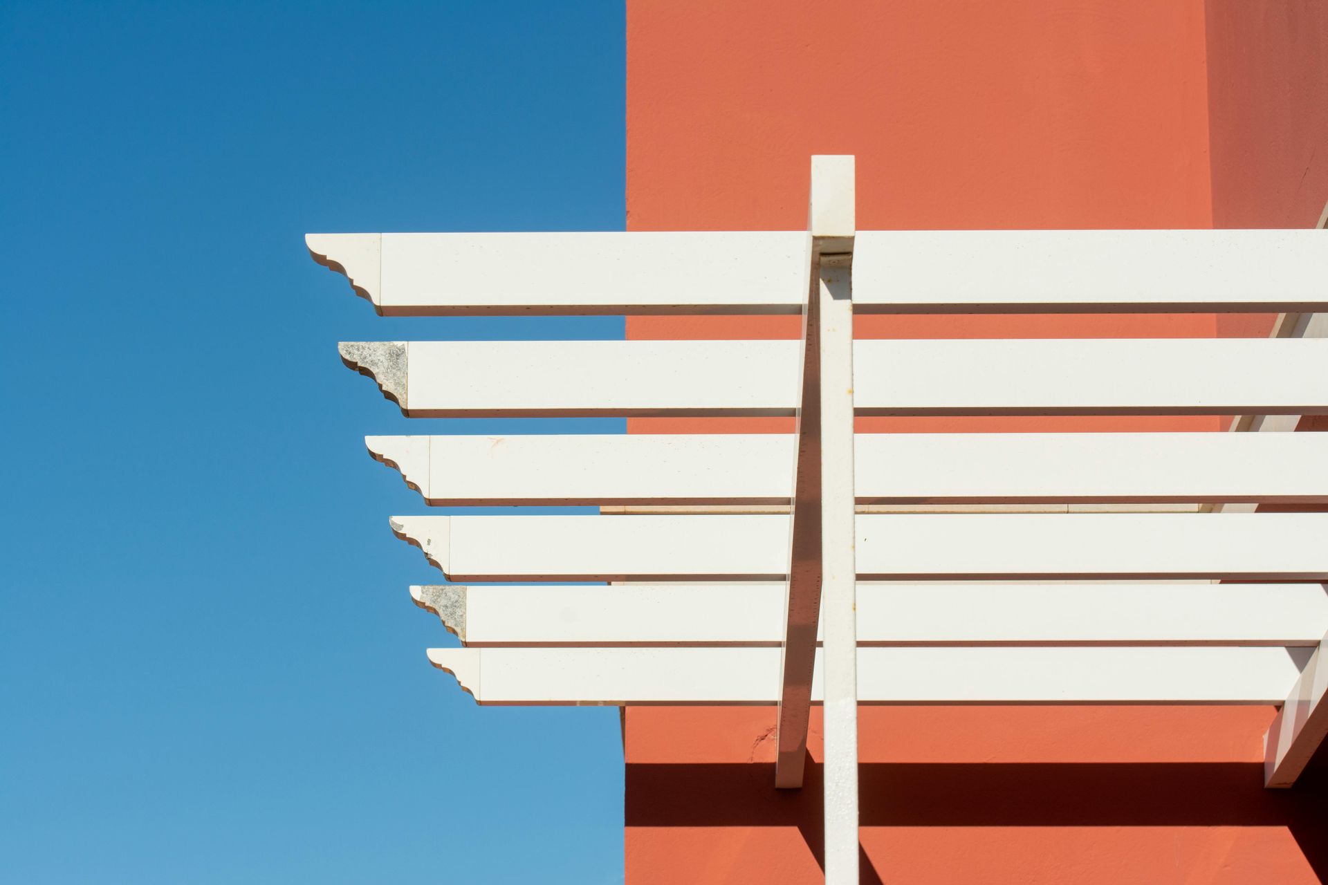 White pergola against a coral wall and blue sky.