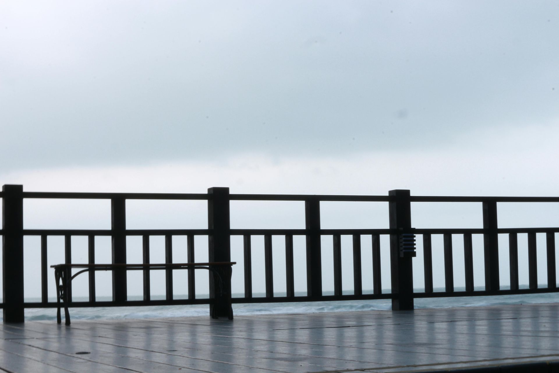 Wooden railing and bench on a deck, overlooking a cloudy, gray seascape.