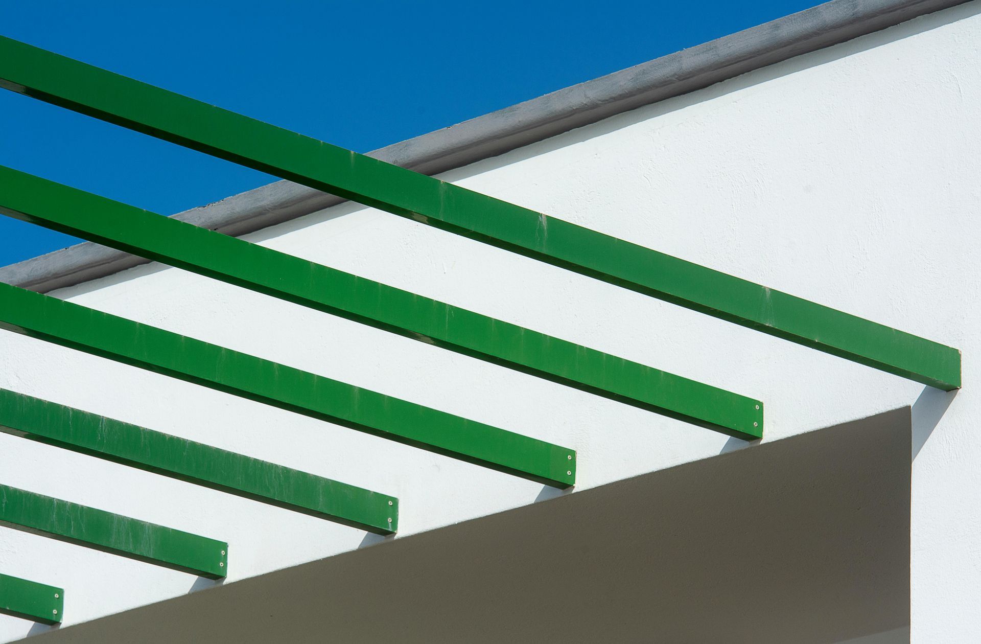 Green beams over white wall against blue sky.