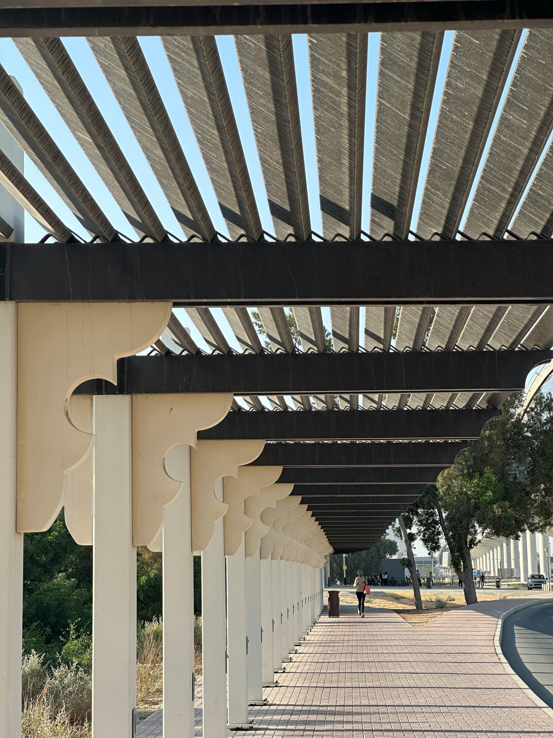 Pergola shading a walkway with a person walking towards the distance. Beige and brown tones.