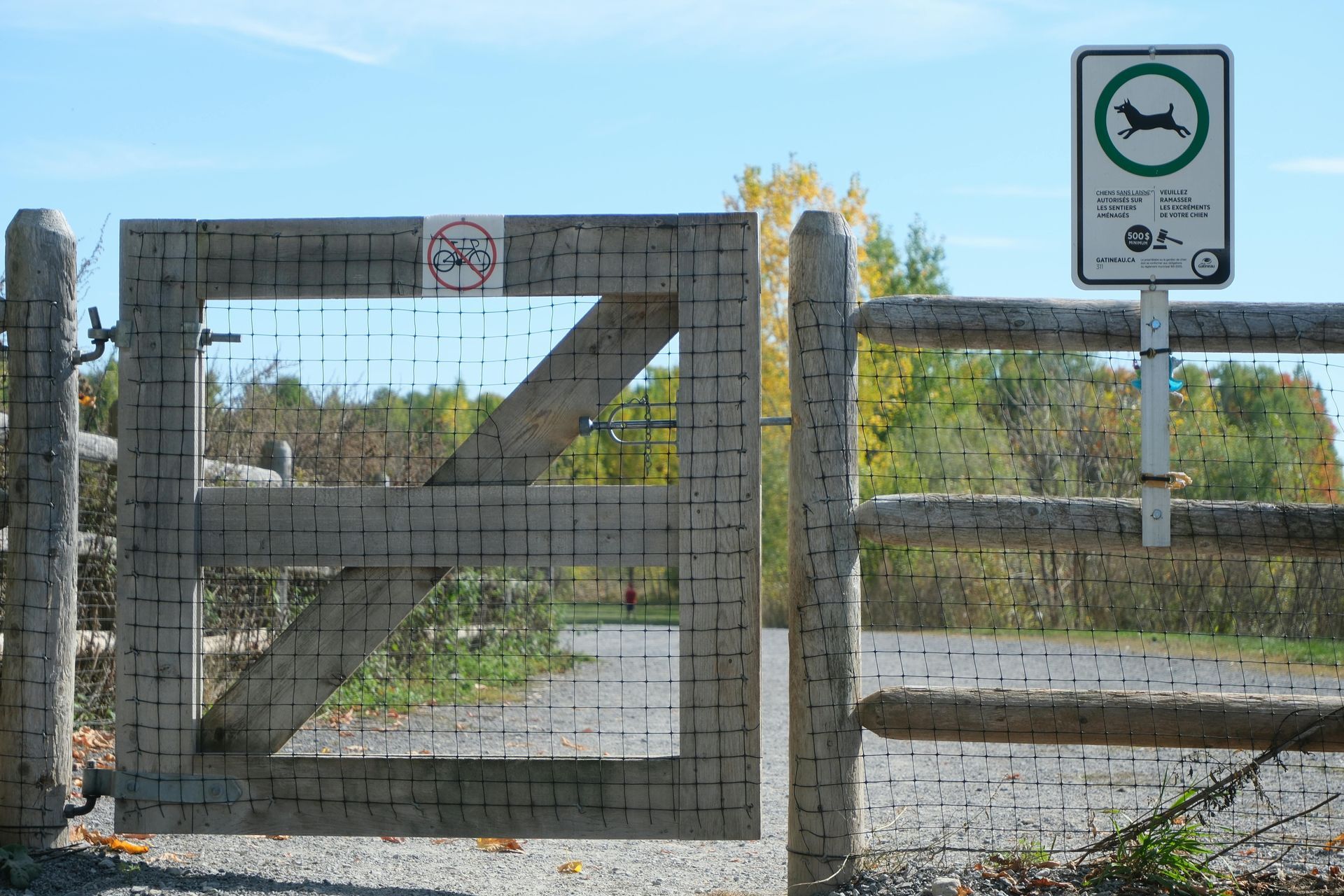 Gate with sign: dogs allowed. No bicycles. Forest background.