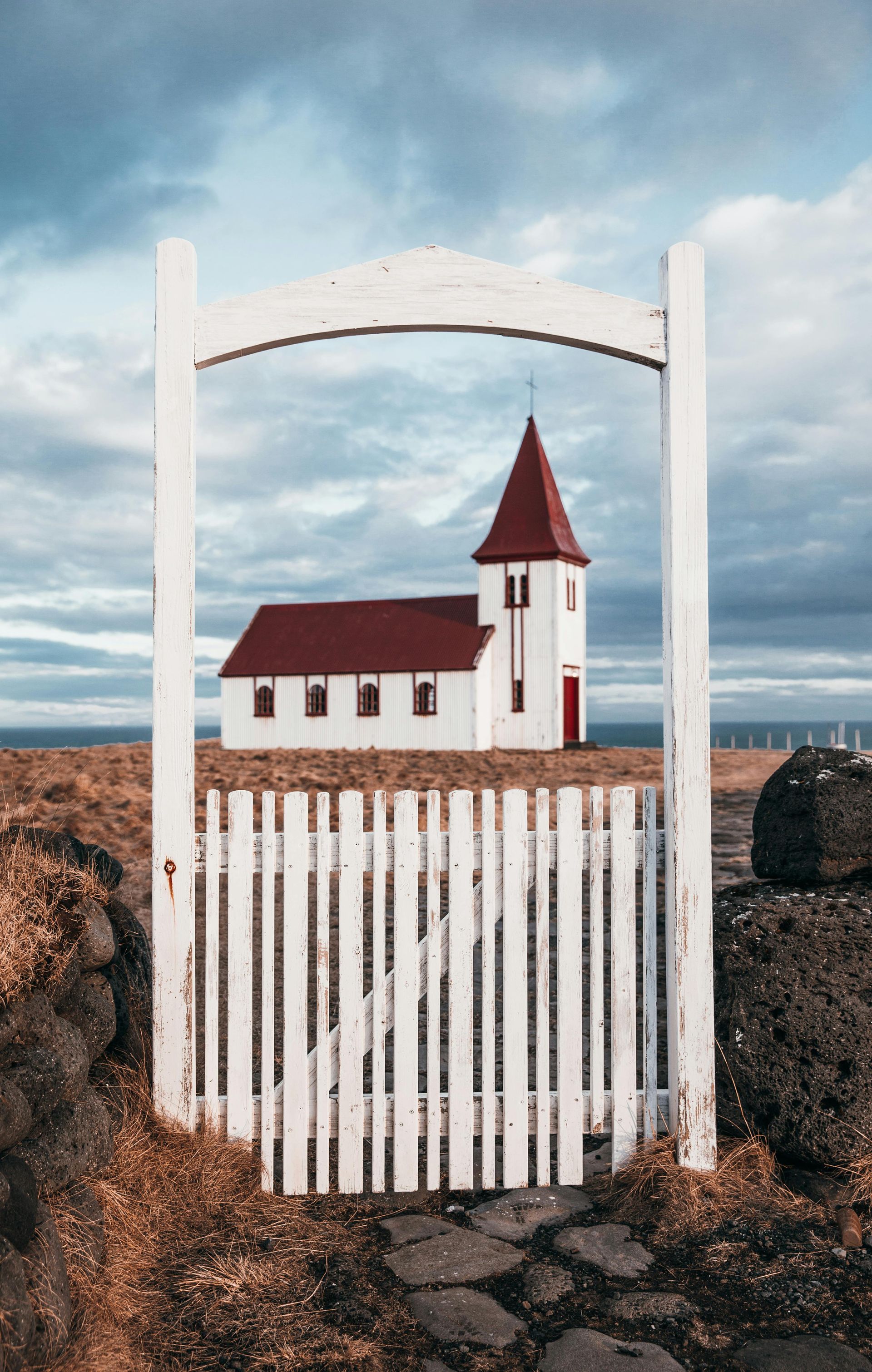 White church with red roof framed by white gate under cloudy sky.