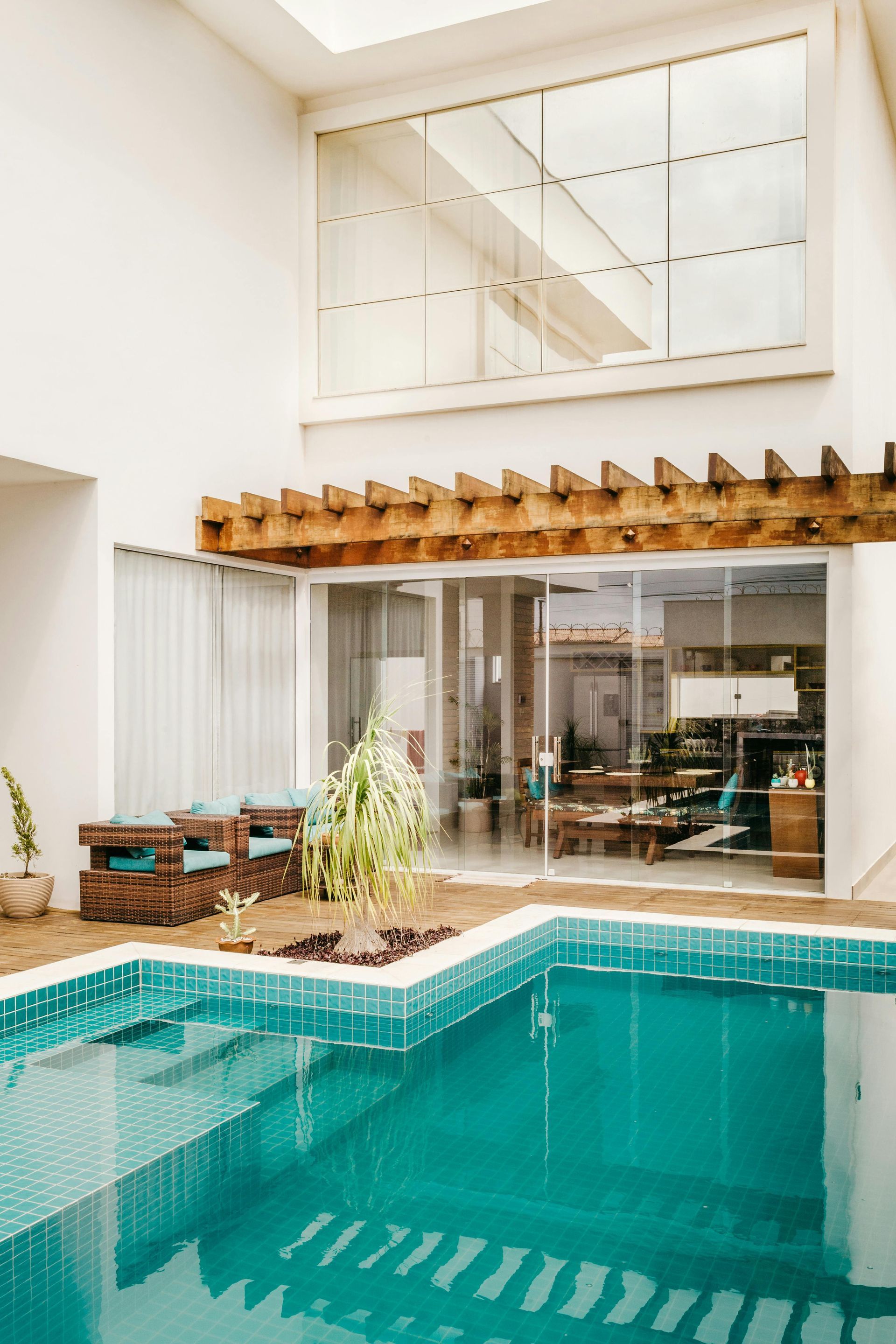 Indoor pool with turquoise water, glass walls, wooden pergola, and seating area.