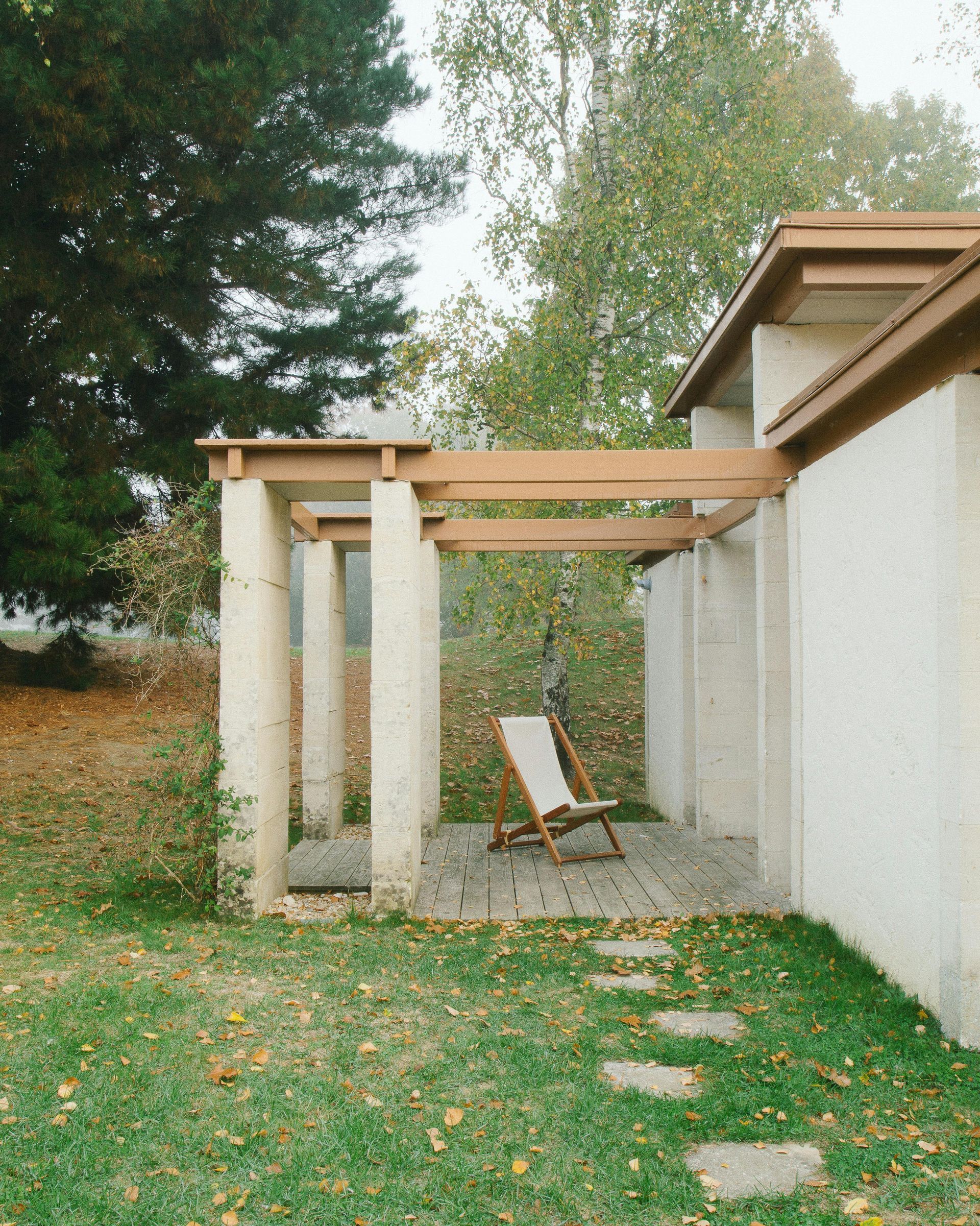 Stone patio with wooden beams, a chair, and stepping stones on grass.