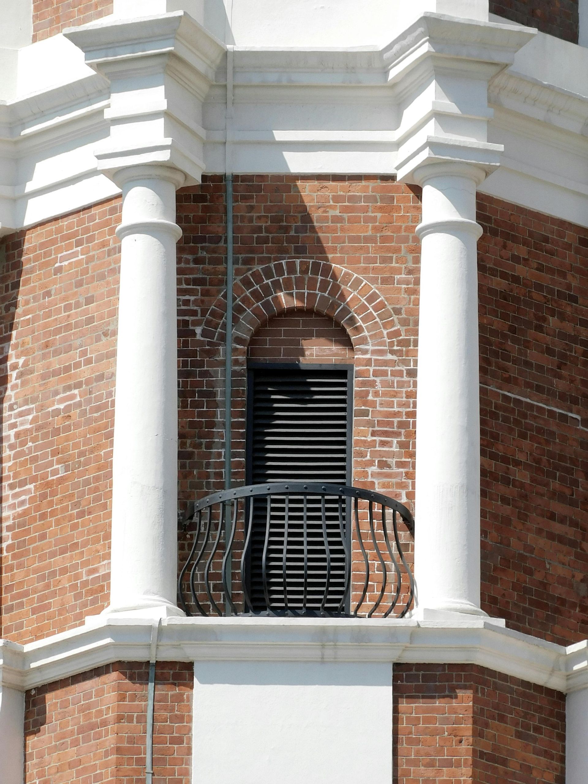 Brick tower with white columns, arched window with black shutters, and decorative black railing.