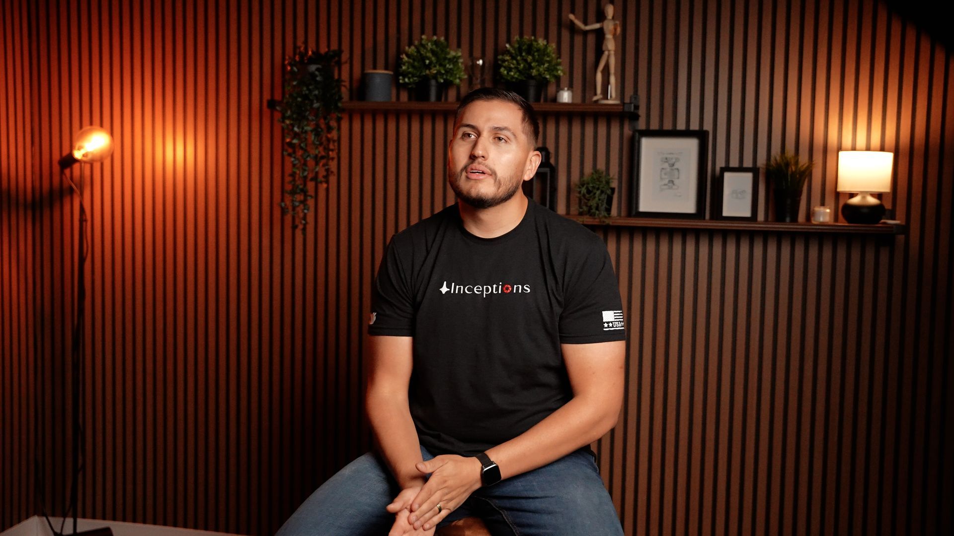 A man is sitting on a stool in a room with a wooden wall.