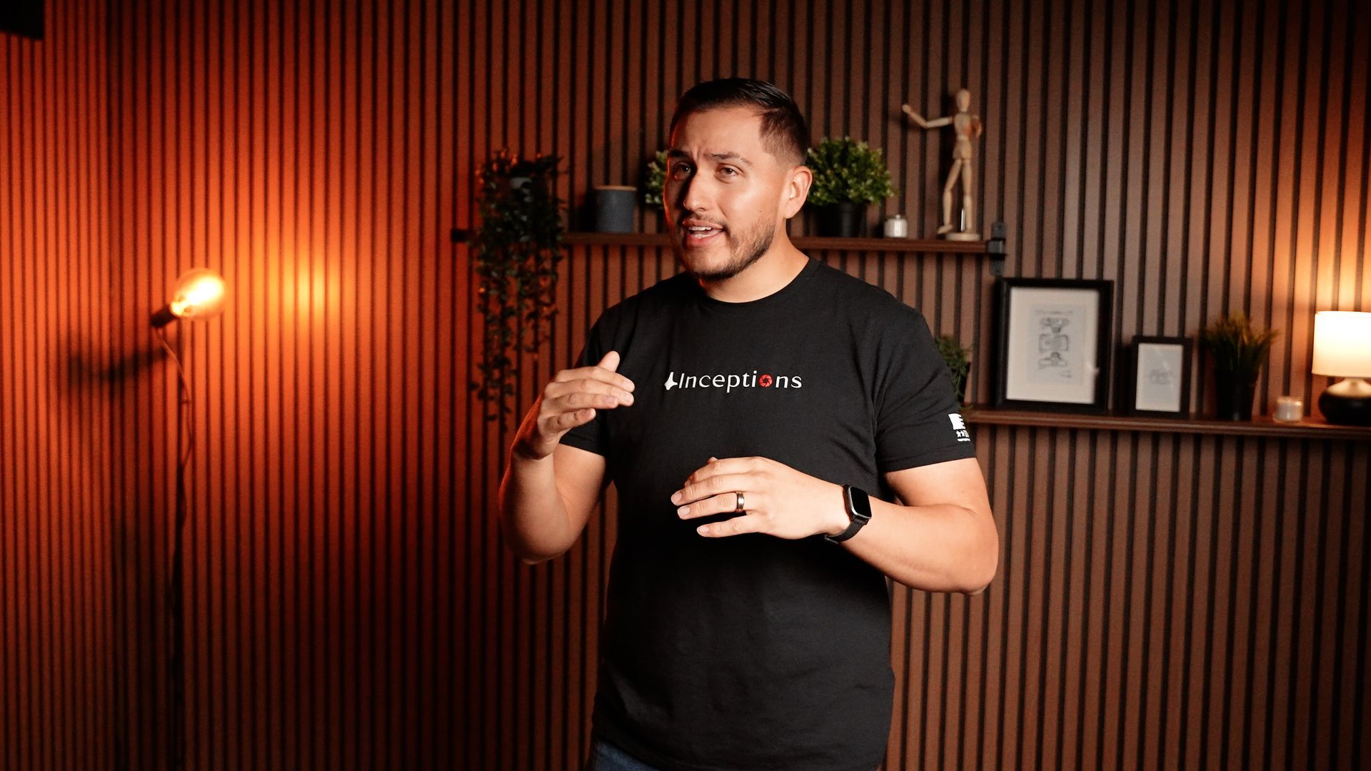 A man in a black t-shirt is standing in front of a wooden wall.