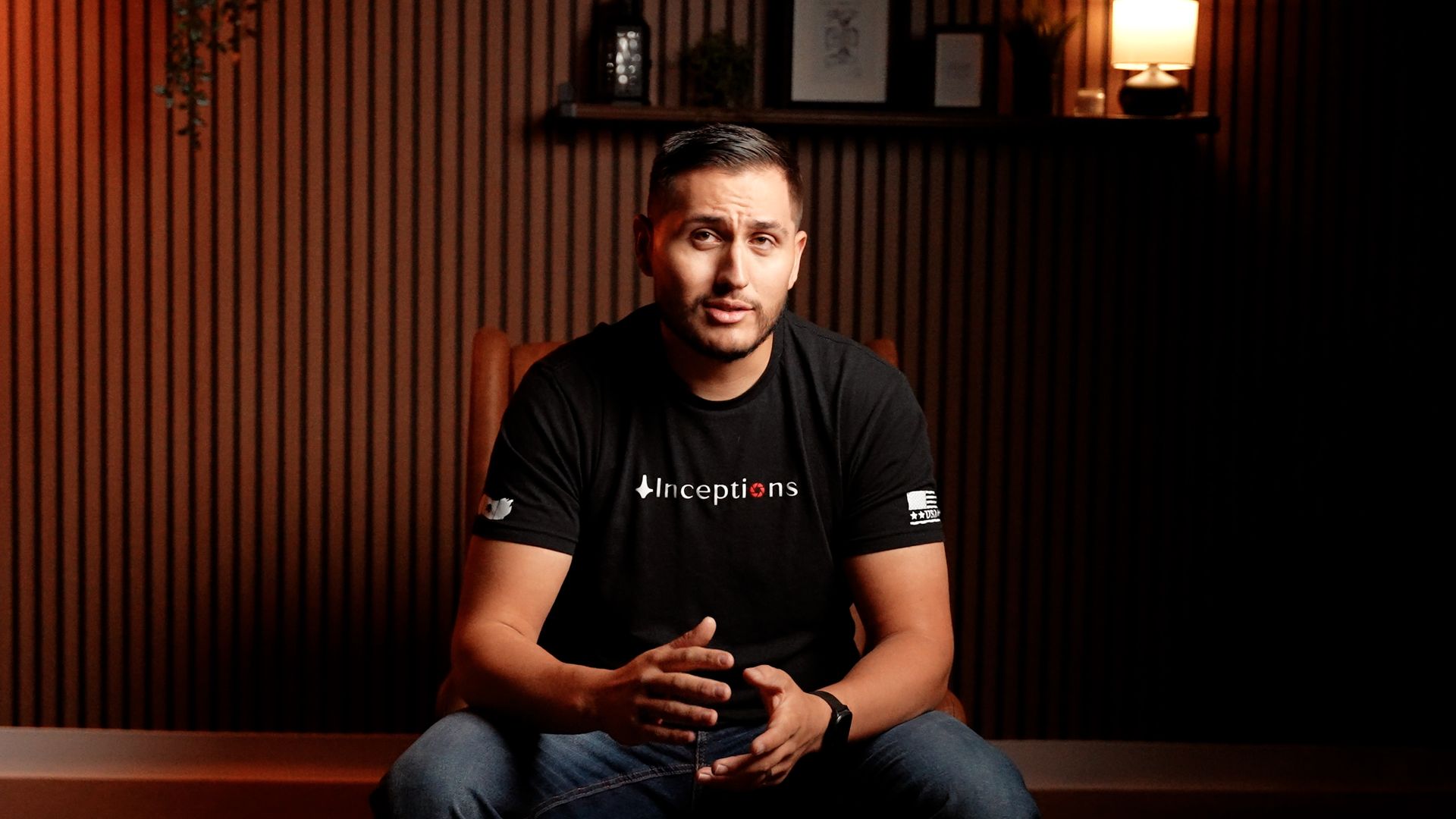 A man in a black t-shirt is sitting on a bench in a dark room.