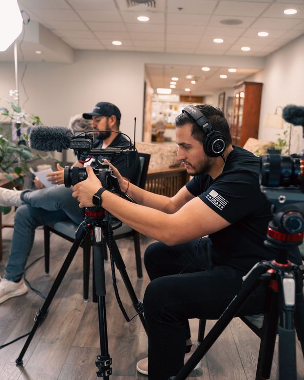 A man wearing headphones is sitting in front of a camera.