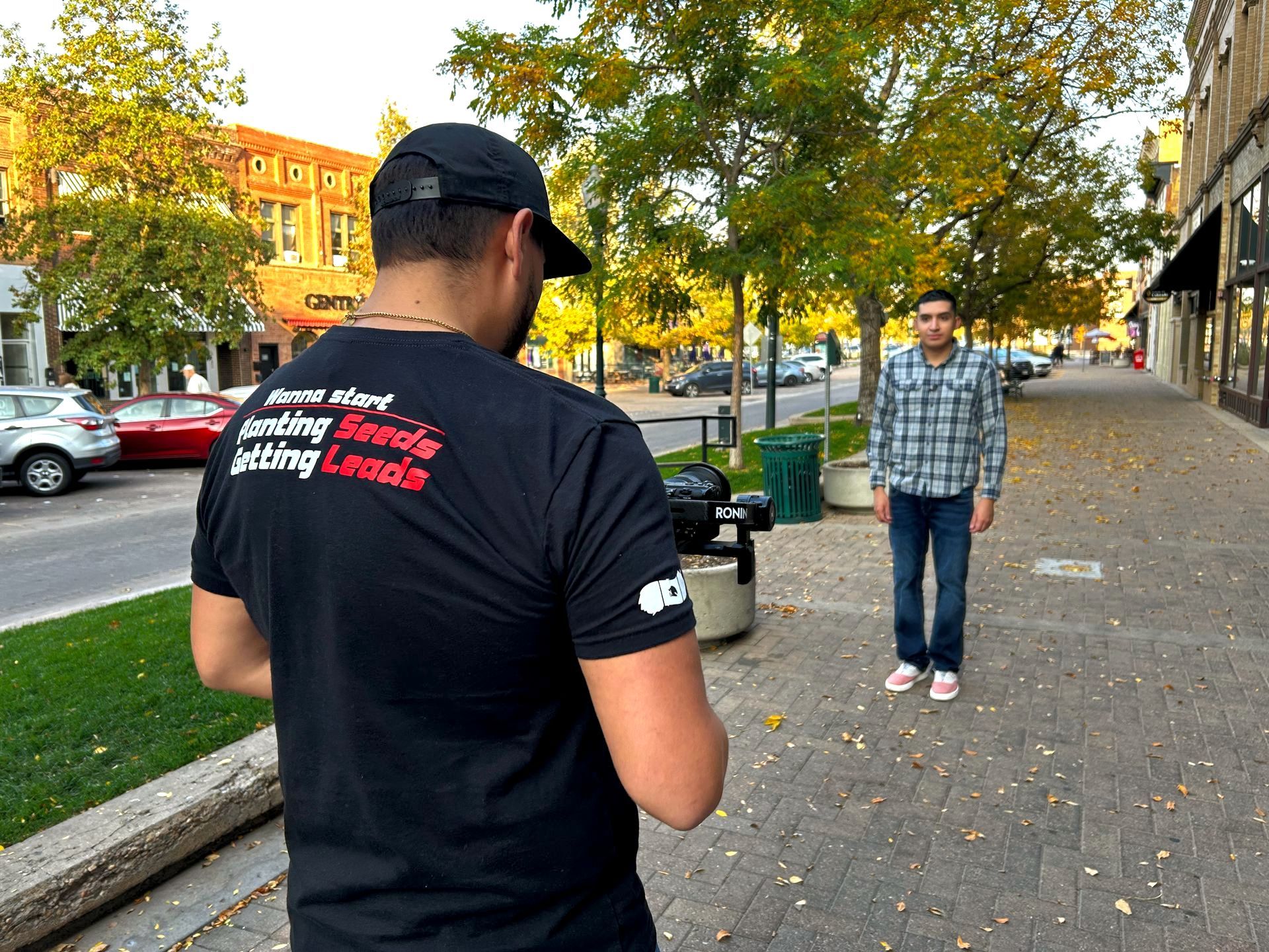 Erick Filming taking a picture of another man on a sidewalk