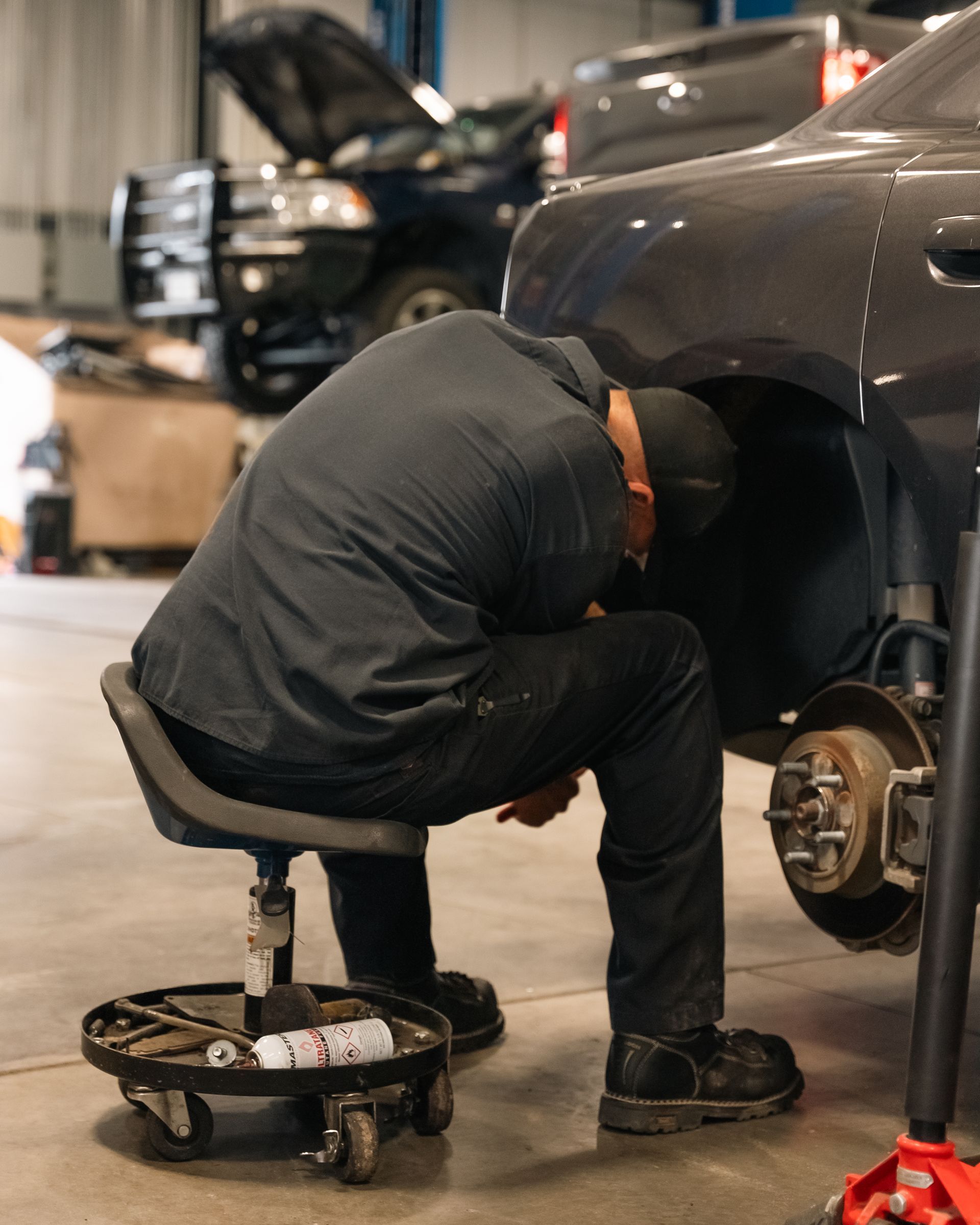A man is kneeling down to work on a car in a garage.
