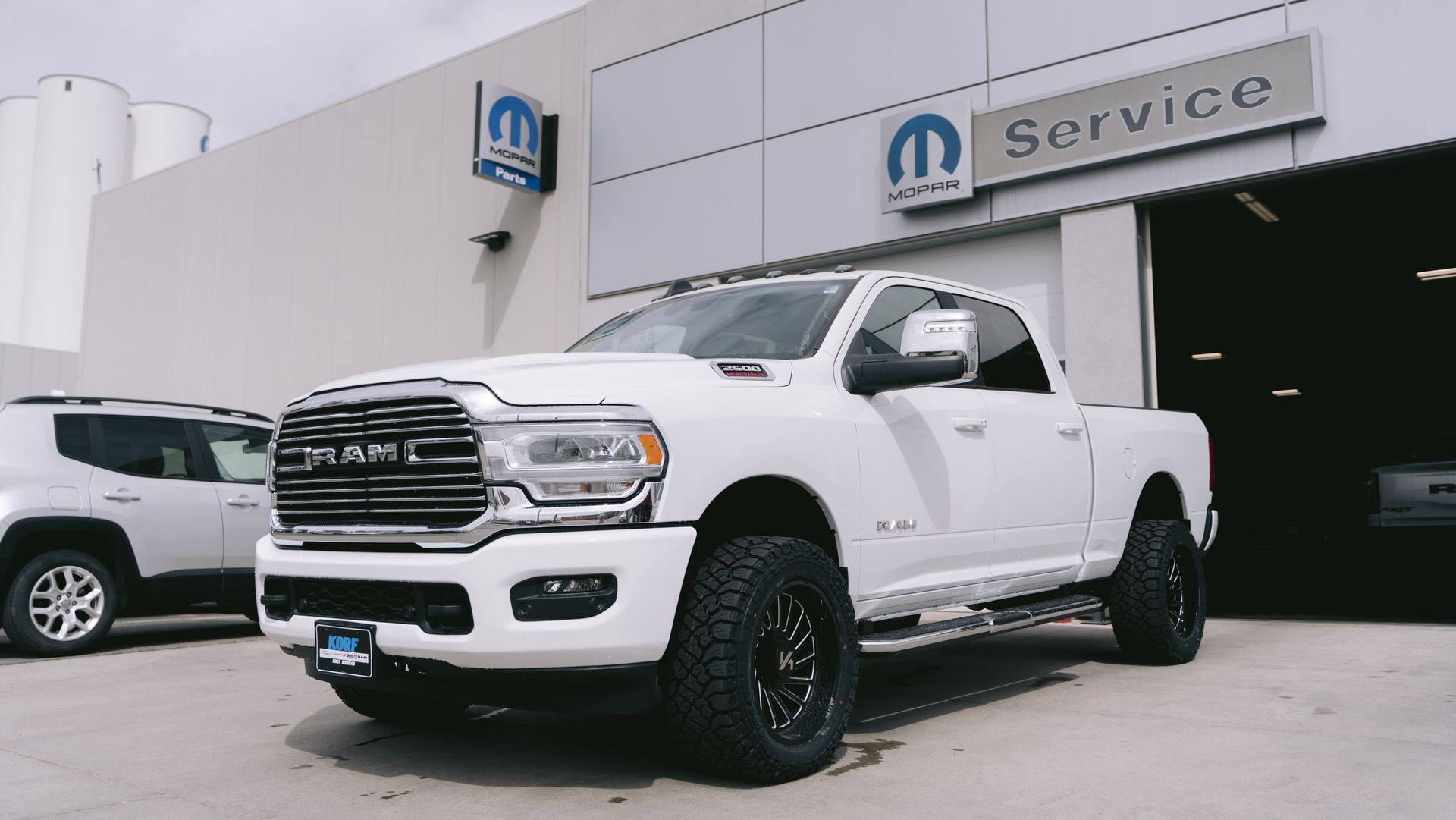 A white ram truck is parked in front of a dodge service center.