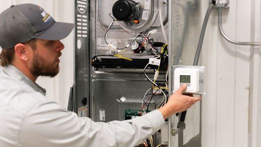 A man is working on a heating system while holding a thermostat.