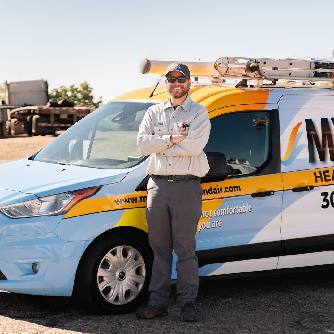 A man is standing in front of a van that says my heating