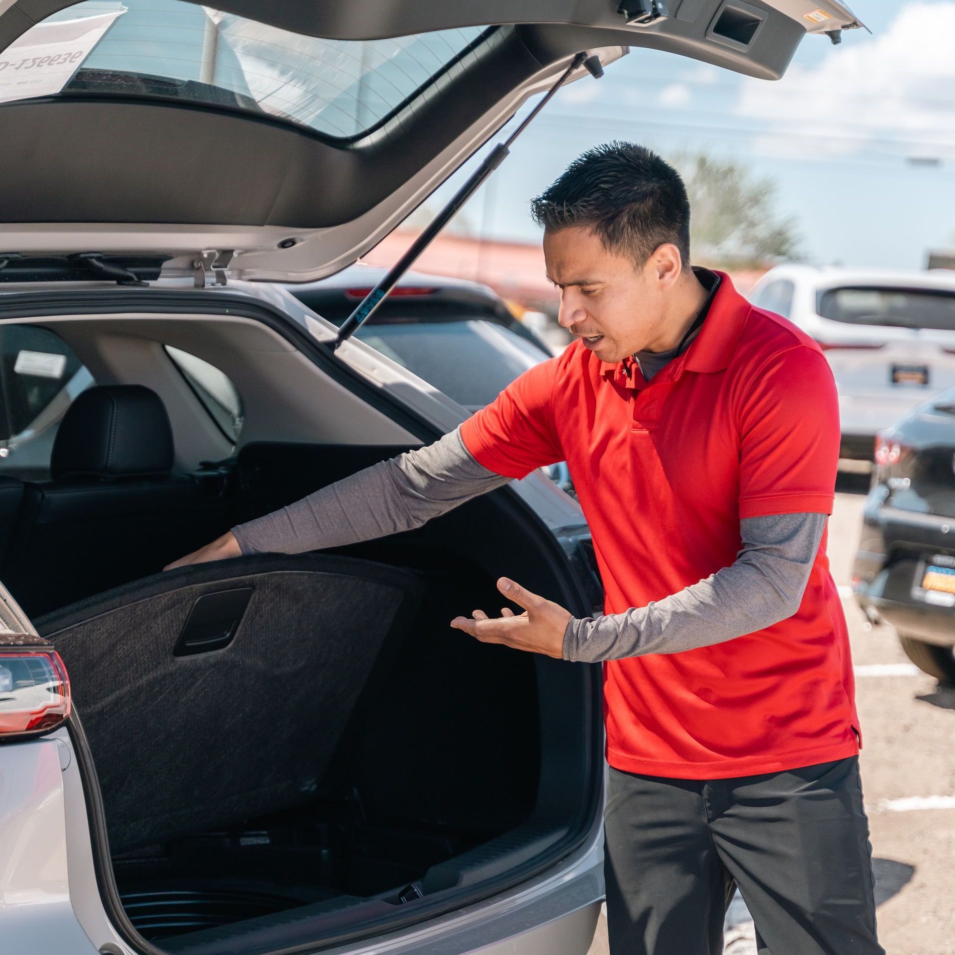 A man in a red shirt is opening the trunk of a car.