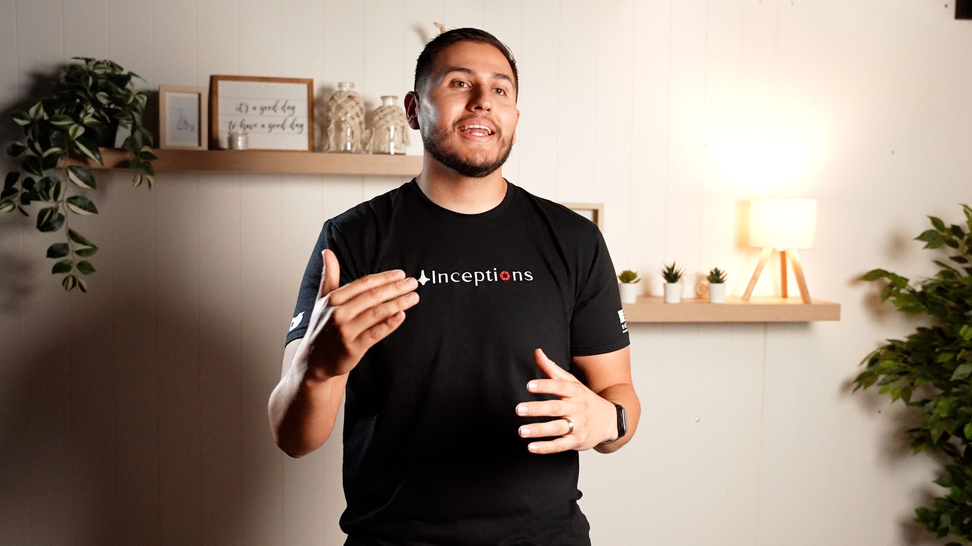 A man in a black t-shirt is standing in a living room with his hands outstretched.